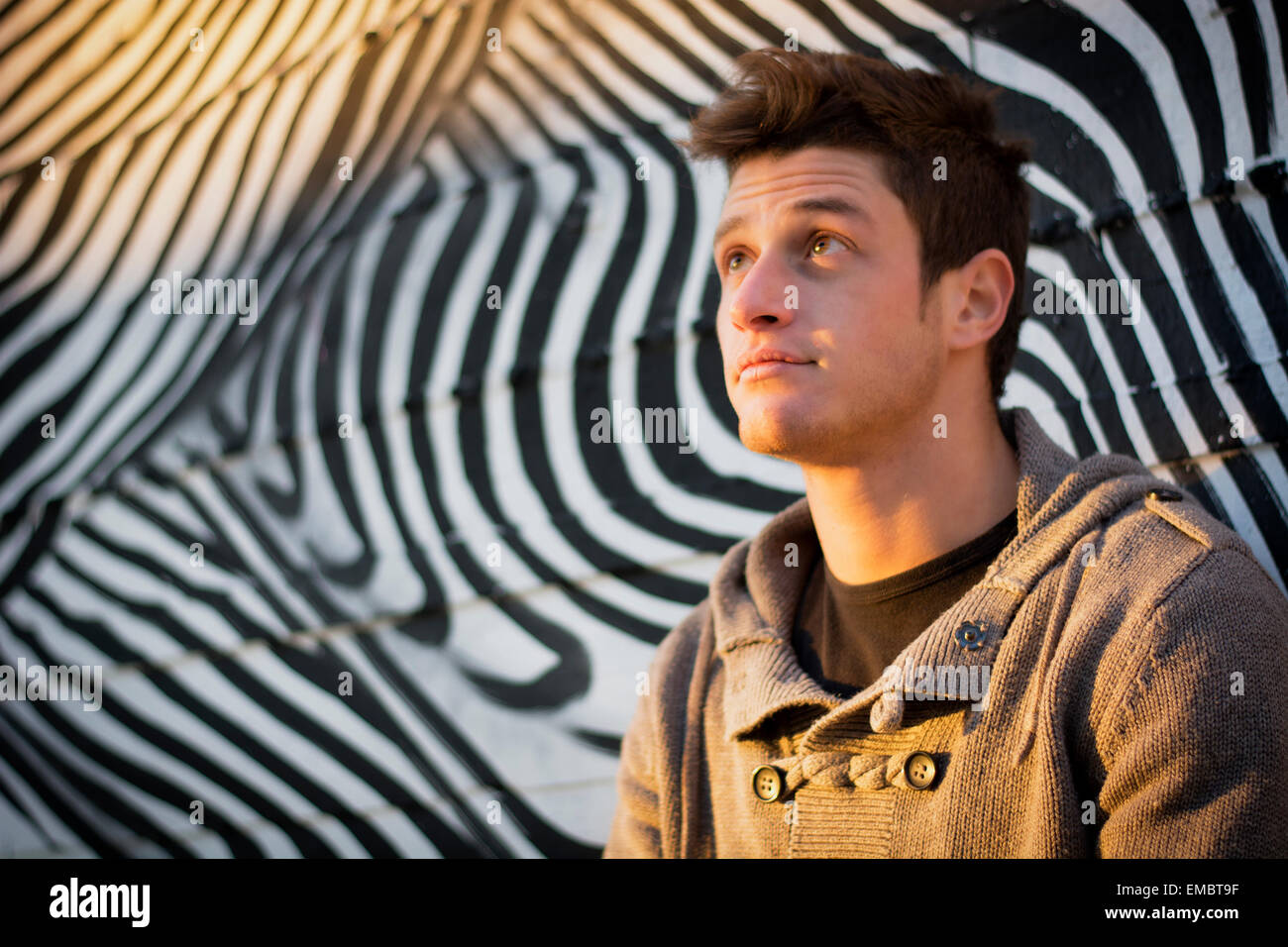 Attraente giovane uomo in piedi contro zebra pattern muro di graffiti, guardando verso l'alto Foto Stock