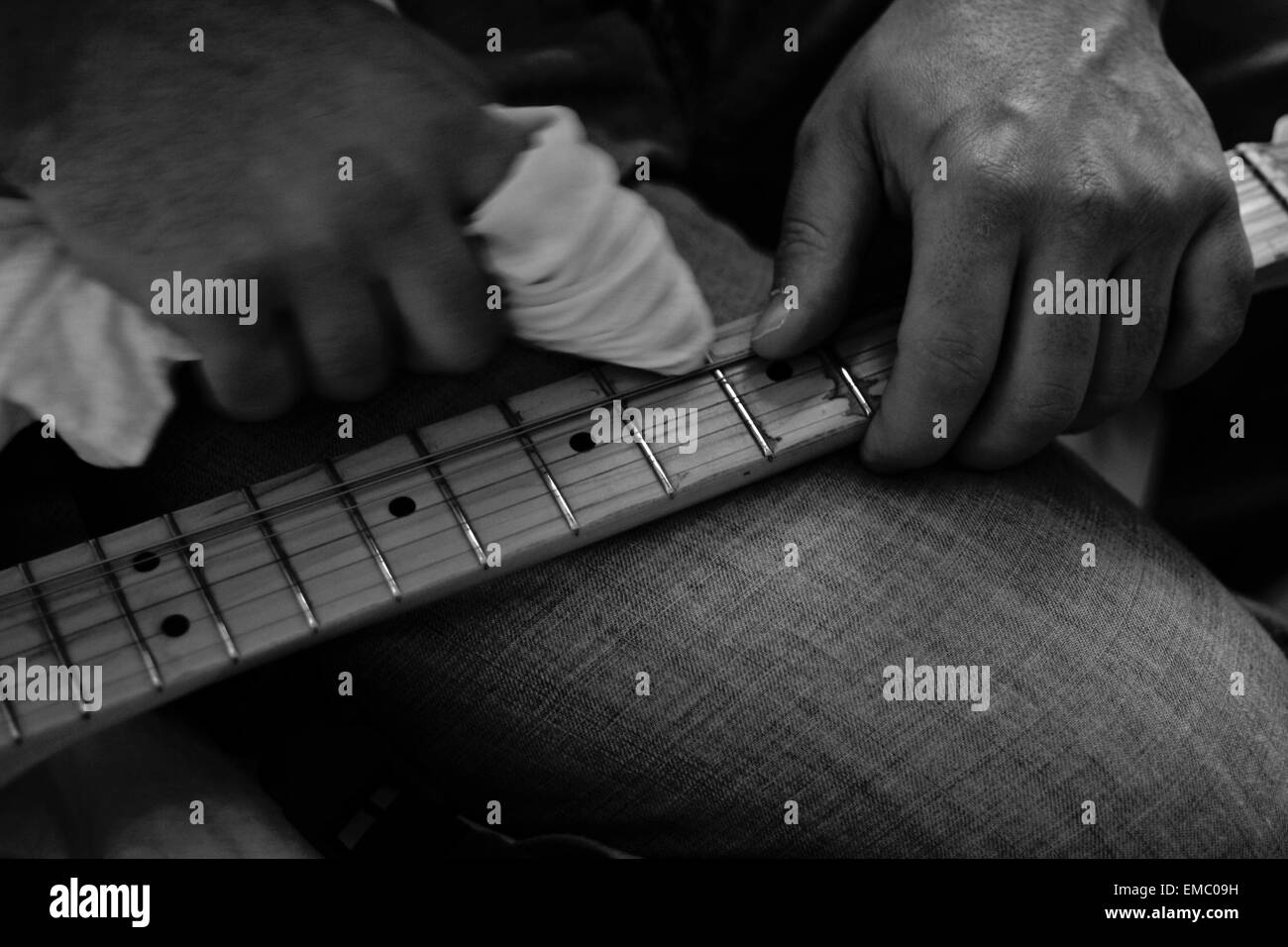 Unidentified uomo pulisce la sua chitarra elettrica il collo con uno straccio bianco sulle ginocchia. Bianco e nero shot Foto Stock