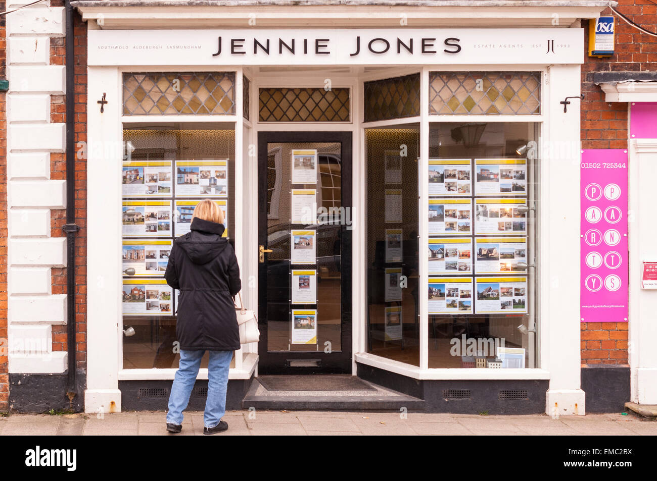 Una donna che guarda in Jennie Jones agente immobiliare nella finestra Southwold , Suffolk , Inghilterra , Inghilterra , Regno Unito Foto Stock