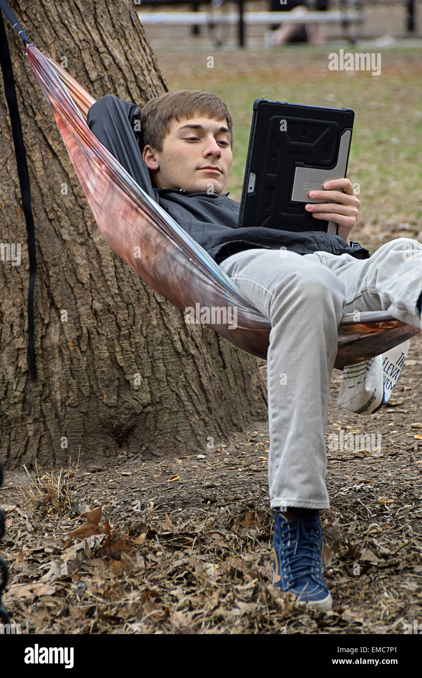 Uno studente di college su un amaca lettura dal suo ipad in Washington Square Park, Greenwich Village di New York City. Foto Stock
