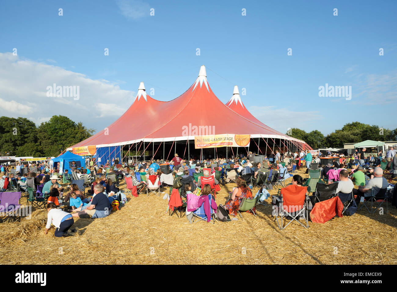 La gente seduta godendo il sole di sera davanti al palco principale al Wickham Music Festival, Hampshire, Inghilterra Foto Stock