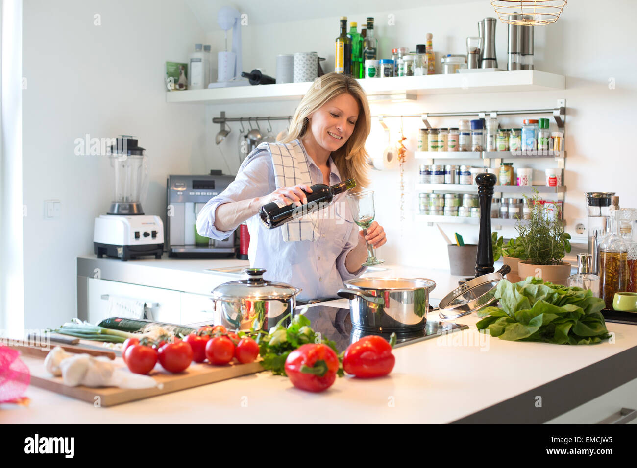 Donna sorridente in cucina versando il vino rosso in vetro Foto Stock