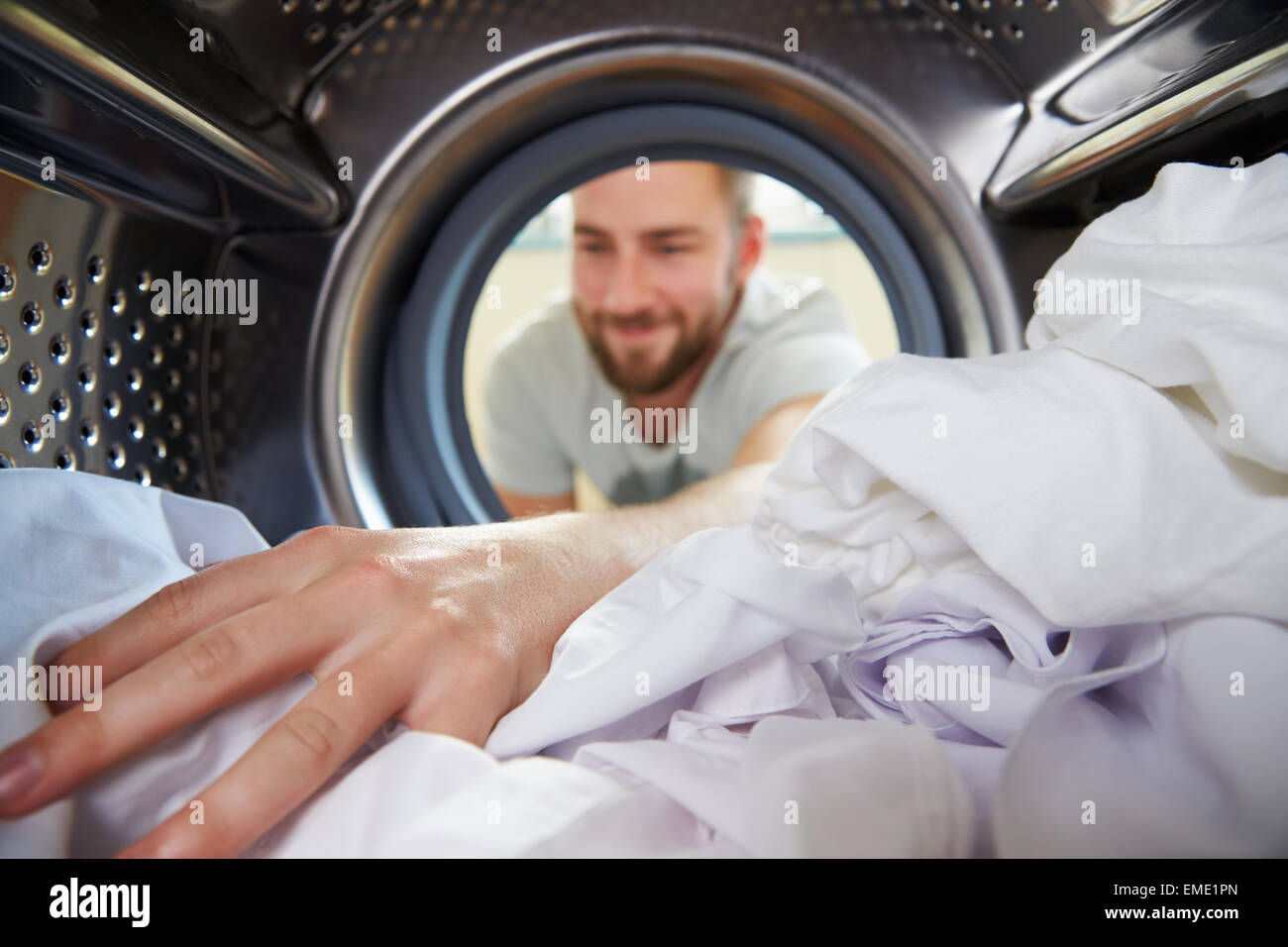 Uomo che fa servizio lavanderia di raggiungere all'interno della macchina di lavaggio Foto Stock