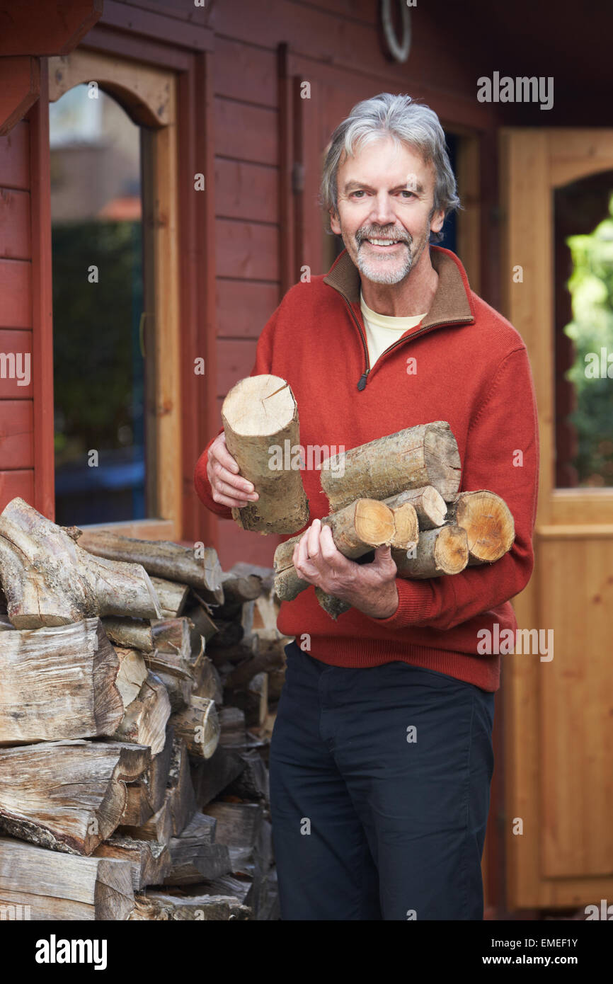 Uomo maturo a raccogliere i log per incendio da Woodpile in giardino Foto Stock