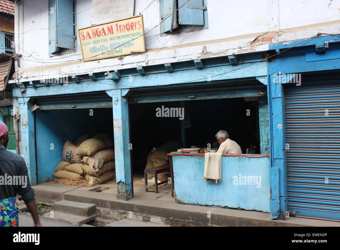 Un vecchio uomo legge un giornale in un aperto fronteggiata godown (magazzino in Mattancherry Foto Stock