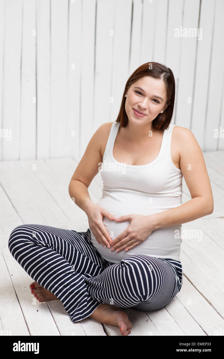 Donna incinta rendendo cuore a mano sul suo ventre Foto Stock