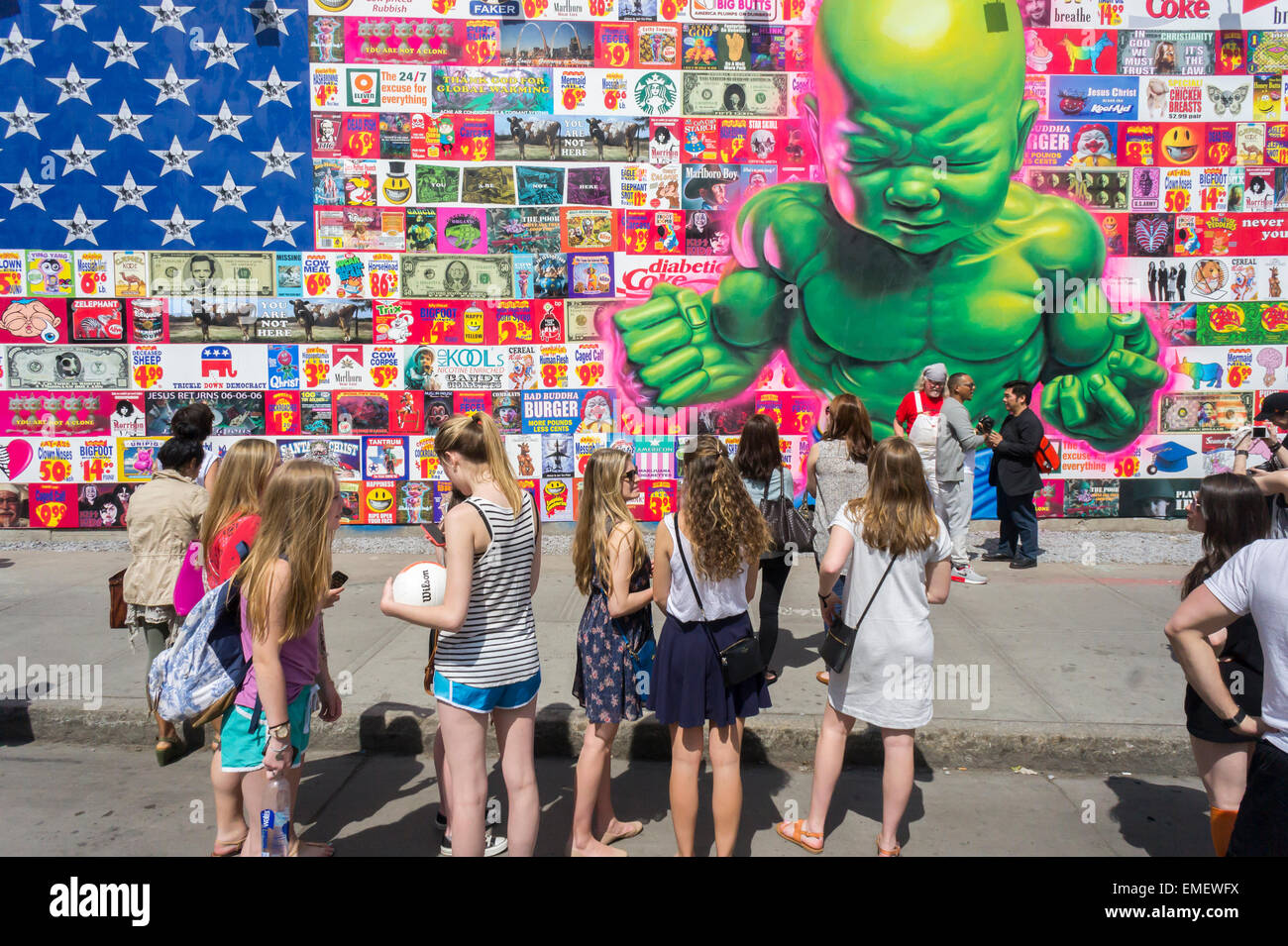 Passer per ammirare il nuovo murale dal famoso artista di strada Ron inglese sul nuovo Bowery murale di Soho a New York sabato 18 aprile, 2015. Inglese di lavoro parodie e critica il consumismo ed è la sua prima opera pubblica da più di un anno. Il ricostruito lo spazio, curata da Jeffrey Deitch, è famoso per ospitare i murali da artisti di graffiti, più segnatamente Keith Haring . (© Richard B. Levine) Foto Stock