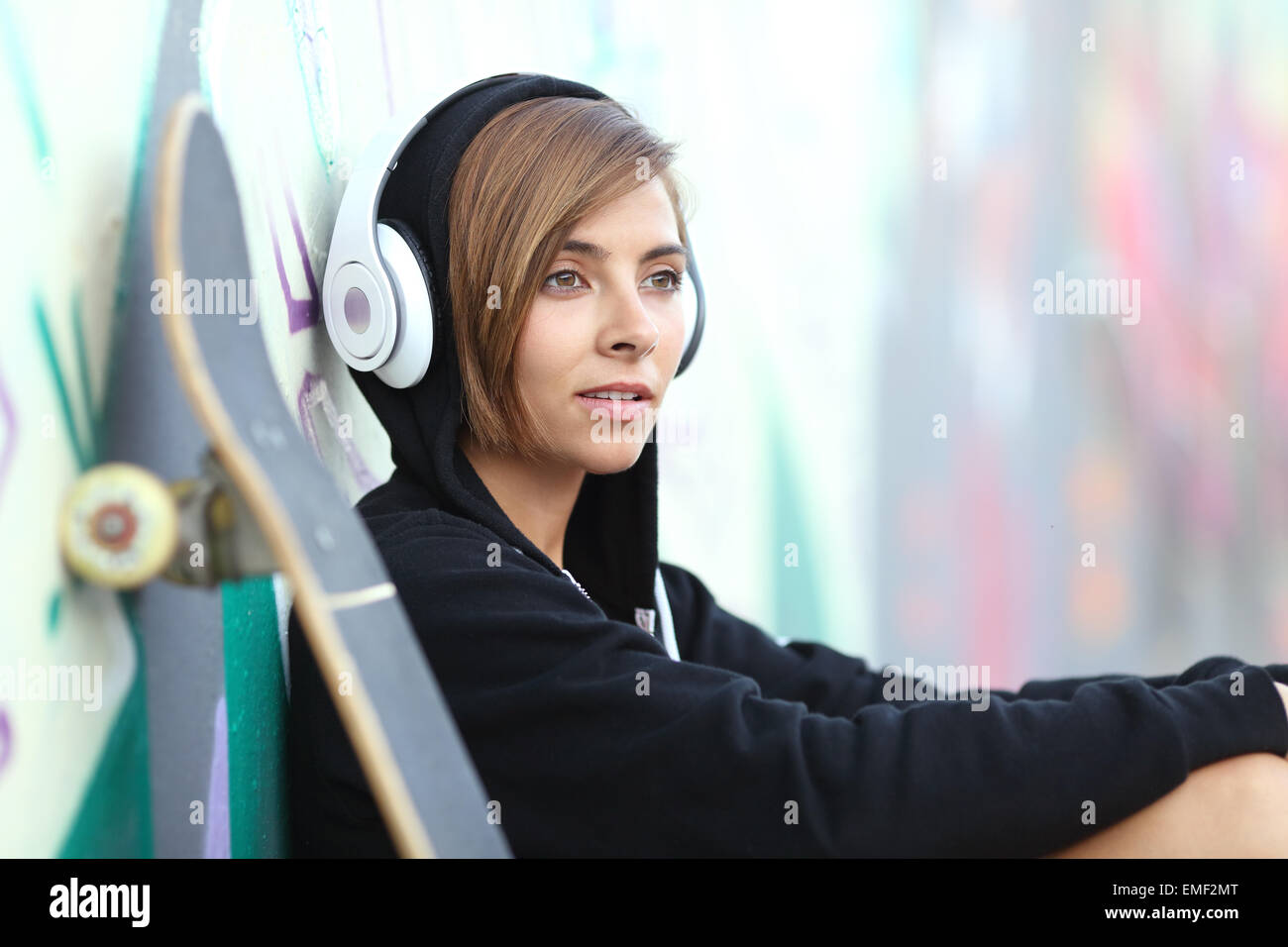 Il giovane skater girl ascoltando la musica con le cuffie con una offuscata muro di graffiti in background Foto Stock