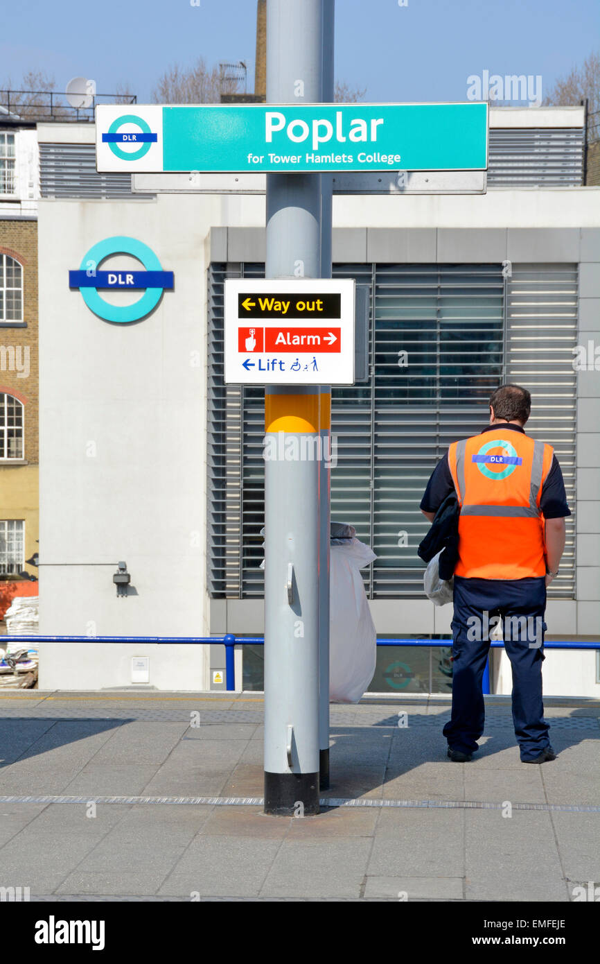Dipendente con vista posteriore Docklands Light Railway in piedi sulla piattaforma Poplar Station che indossa un giubbotto ad alta visibilità con deposito DLR e logo oltre Londra UK Foto Stock