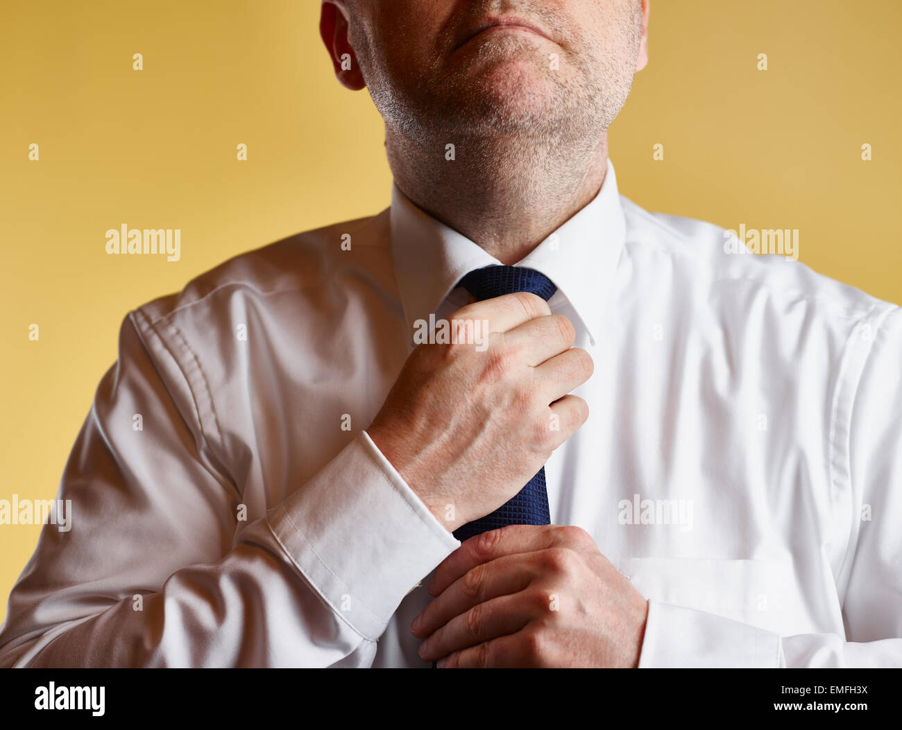 Close up, maschio che indossa una camicia bianca e cravatta blu, egli serrare il nodo di cravatta, sfondo giallo Foto Stock