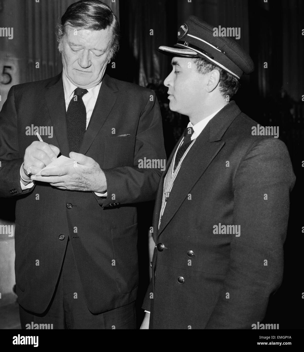 Attore americano John Wayne lasciando il Ambassadeurs Club di Hamilton Place, Londra segni un autografo per portiere Tas ontano. Il 17 gennaio 1974. Foto Stock