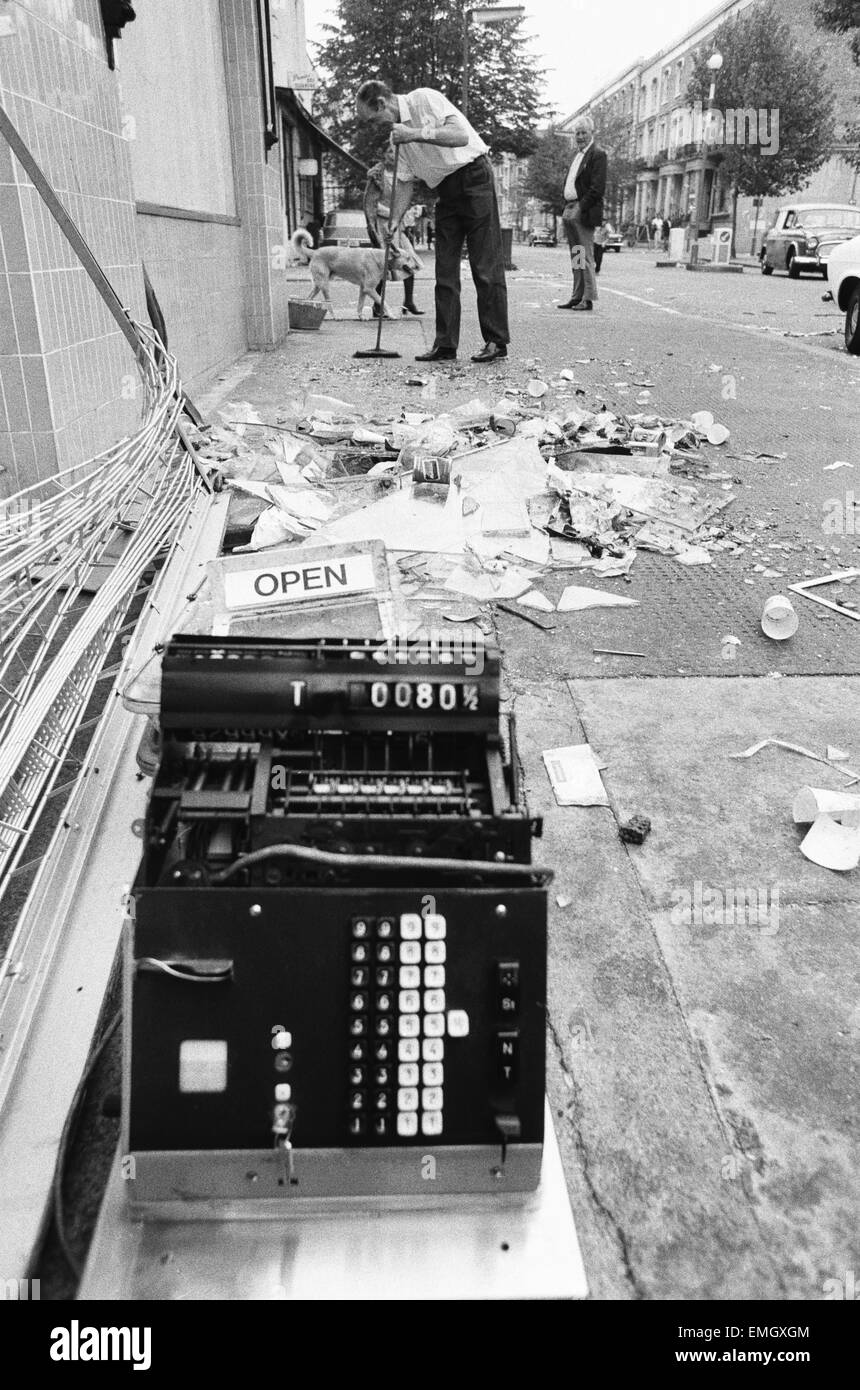 Un Co-op lavoratore comincia il grande compito di spazzare i detriti dopo lunedì notte di disordini nelle strade di Notting Hill, West London. in primo piano è un fracassato registratore di cassa dal negozio. Il 31 agosto 1976. Foto Stock
