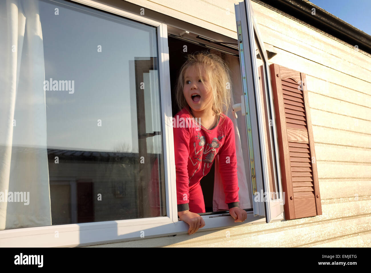 Una giovane ragazza in pigiama guarda fuori dalla finestra di una roulotte all inizio di un nuovo giorno Foto Stock