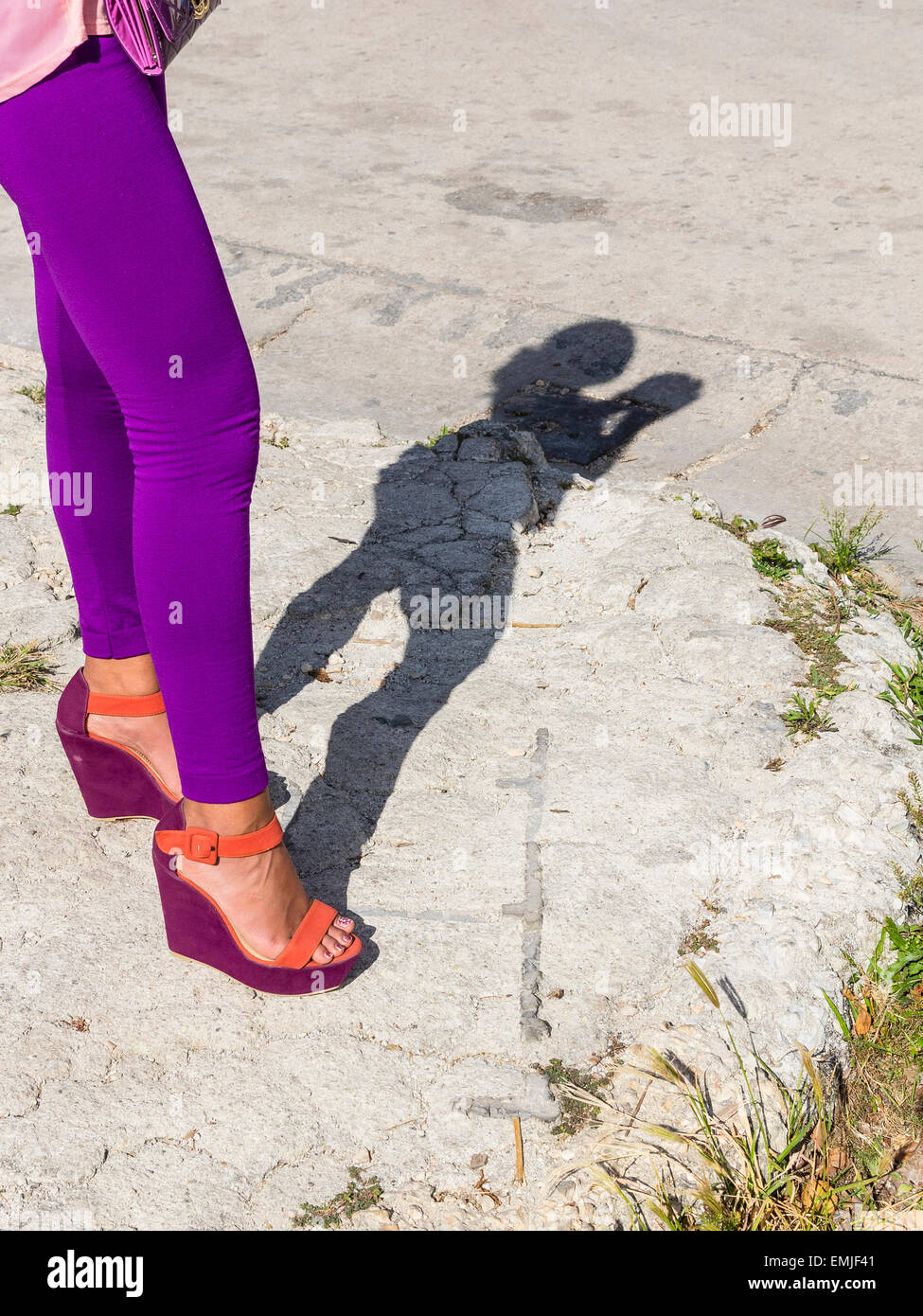 Una immagine di una donna collant color porpora, dalla vita in giù e viola e arancione scarpe. La donna getta a figura intera ombra. Foto Stock