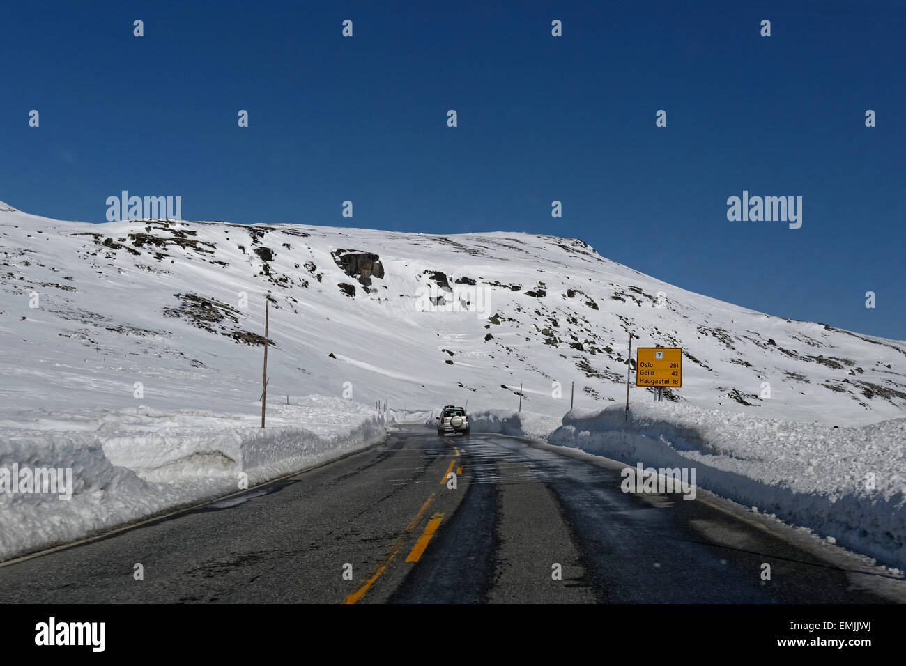 Guida auto in direzione est sulla strada E7 su Hardangervidda, Norvegia, con alte mura di neve che circonda la strada. Foto Stock