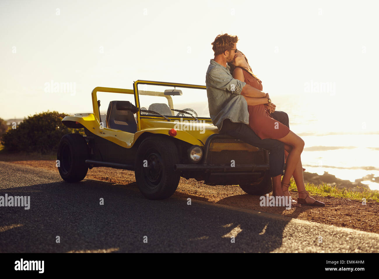 Romantico coppia giovane seduto sul cofano della loro auto e baciare. Coppia giovane la condivisione di un appassionato bacio sul viaggio. Foto Stock