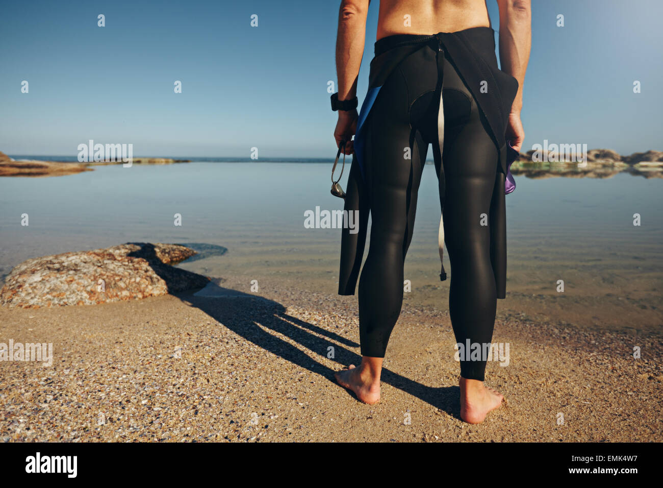 Vista posteriore dell'uomo in piedi sul lago di muta da indossare. Tagliate il colpo di un triatleta tenetevi pronti per una gara. Foto Stock