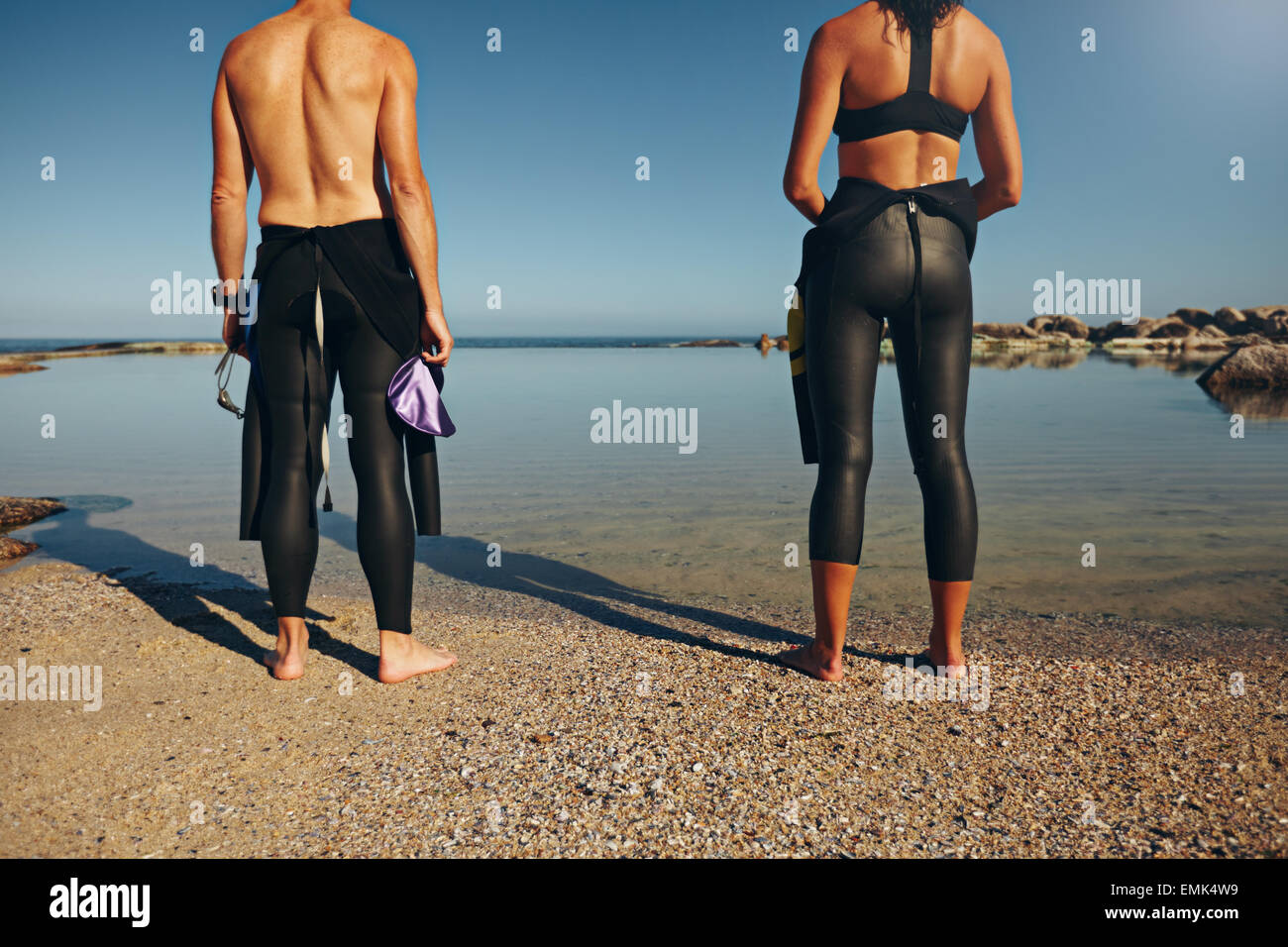 Vista ritagliata di atleti permanente sulla spiaggia della preparazione di una gara. L uomo e la donna la preparazione per il triathlon indossando una muta. Foto Stock