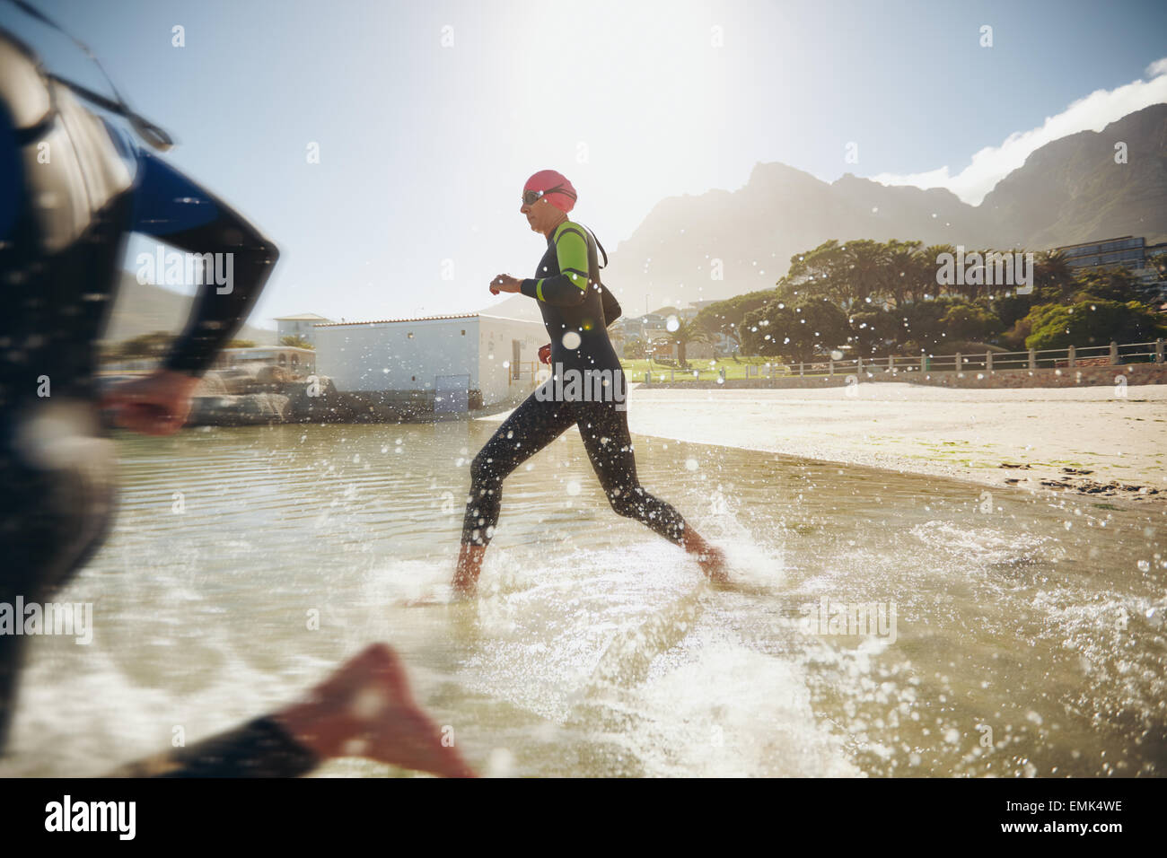 I partecipanti eseguono in acqua per l'avvio di un triathlon. Due triatleti precipitando in acqua. Foto Stock