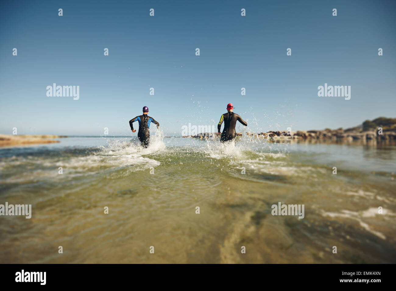 I partecipanti eseguono in acqua per l'avvio di un triathlon. Due triatleti precipitando in acqua per nuotare porzione di gara. Foto Stock