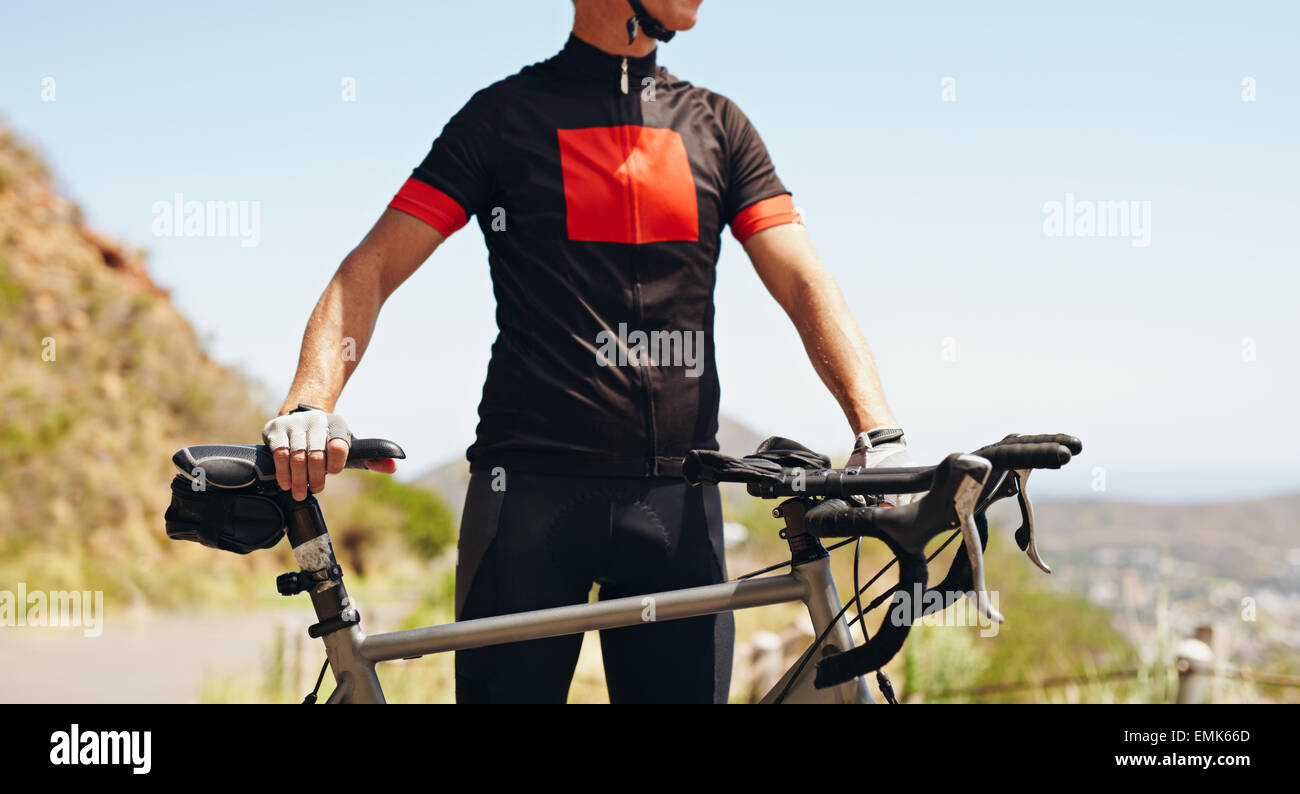 Sezione di metà immagine dell uomo che indossa abbigliamento ciclistico in piedi con la sua bicicletta, all'esterno. Foto Stock