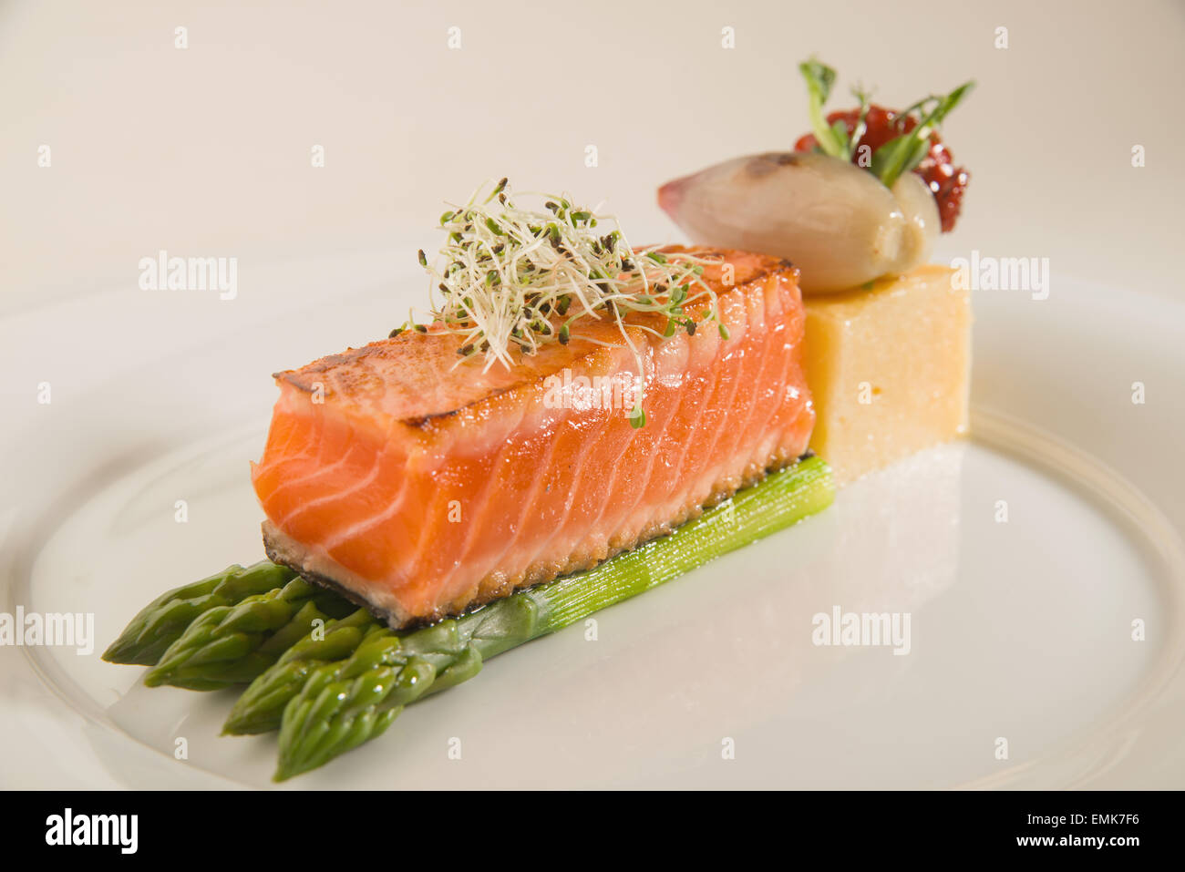 Un pezzo di salmone fritto, asparagi, porridge di mais su una piastra bianca Foto Stock