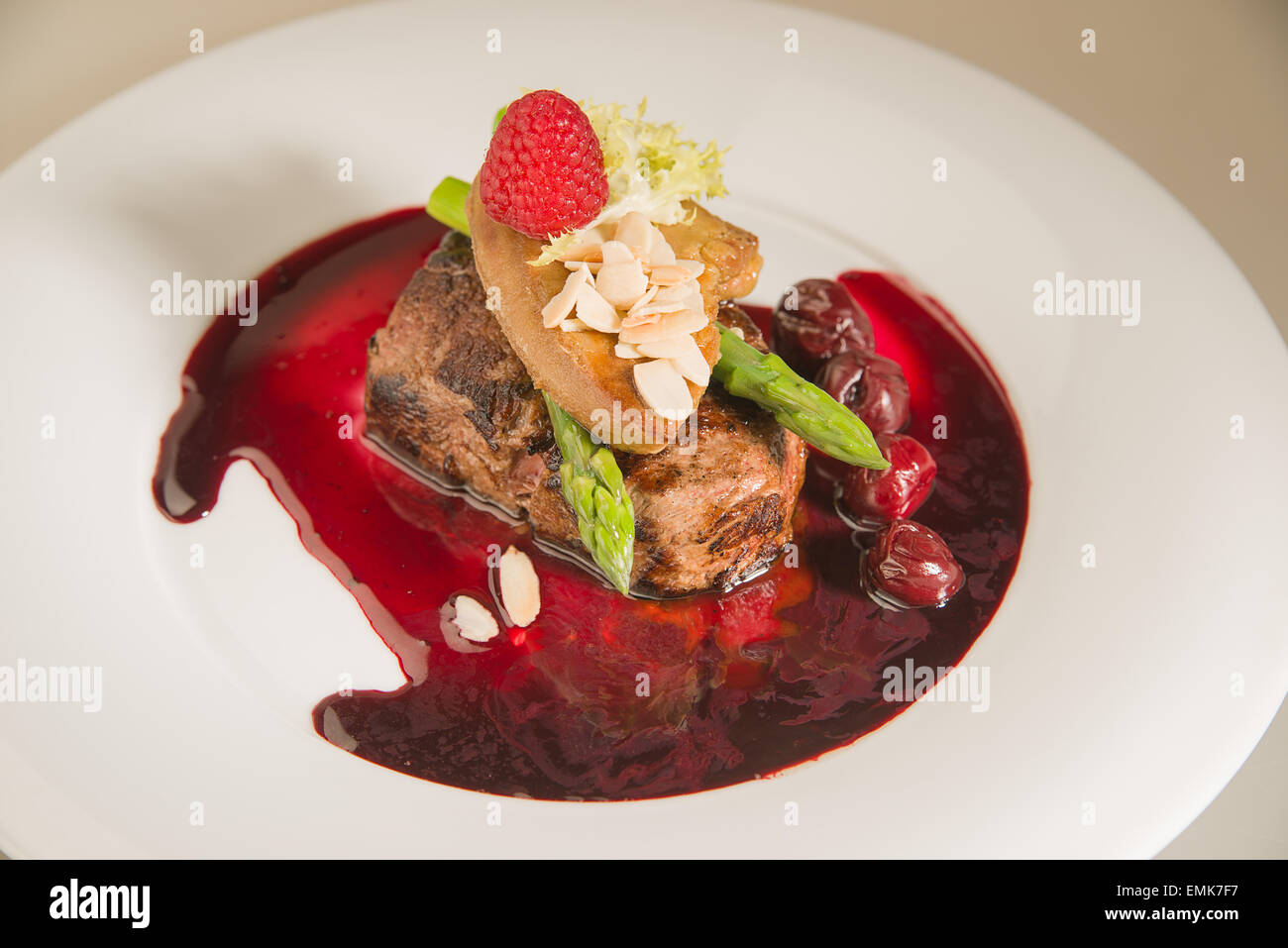 Pezzo di carne arrosto in salsa alle ciliegie, asparagi, lampone su una piastra bianca Foto Stock