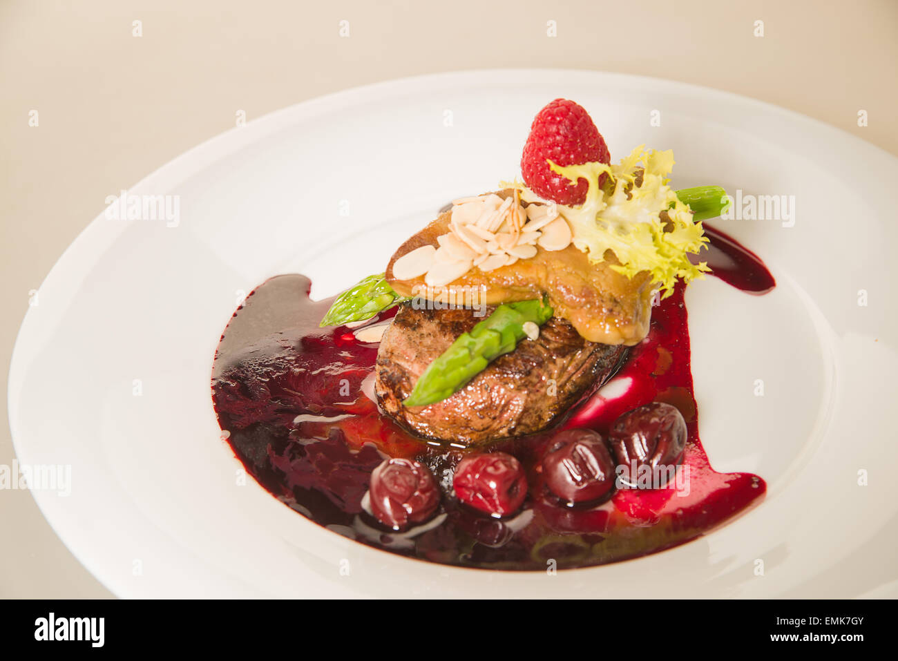 Pezzo di carne arrosto in salsa alle ciliegie, asparagi, lampone su una piastra bianca Foto Stock