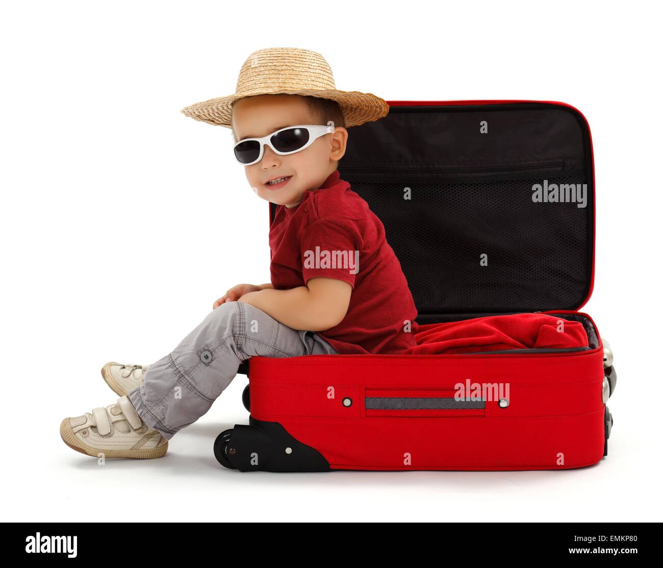 Fiducioso little boy indossando occhiali da sole e cappello di paglia, seduta in valigia aperta Foto Stock