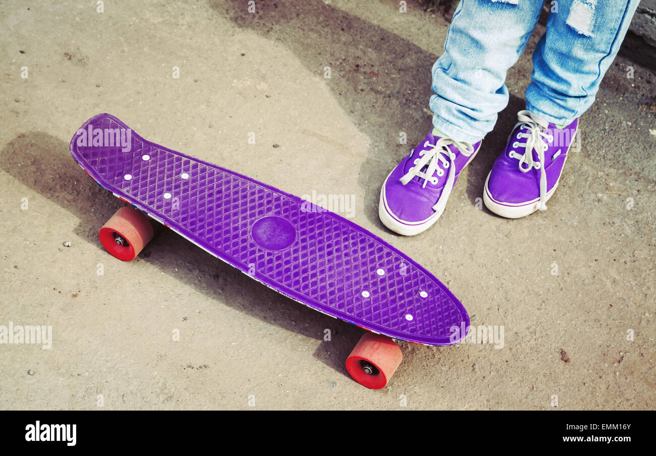 Adolescente in piedi in jeans e snickers con lo skateboard, Photo retrò con correzione delle tonalità, instagram vecchio stile Foto Stock