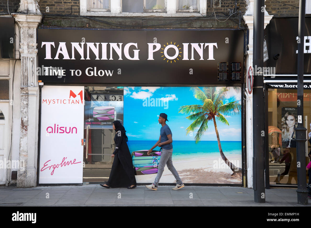 Abbronzante con Palm Tree spiaggia foto murale e persone passato a camminare sul marciapiede compresi donna in abito islamico Foto Stock