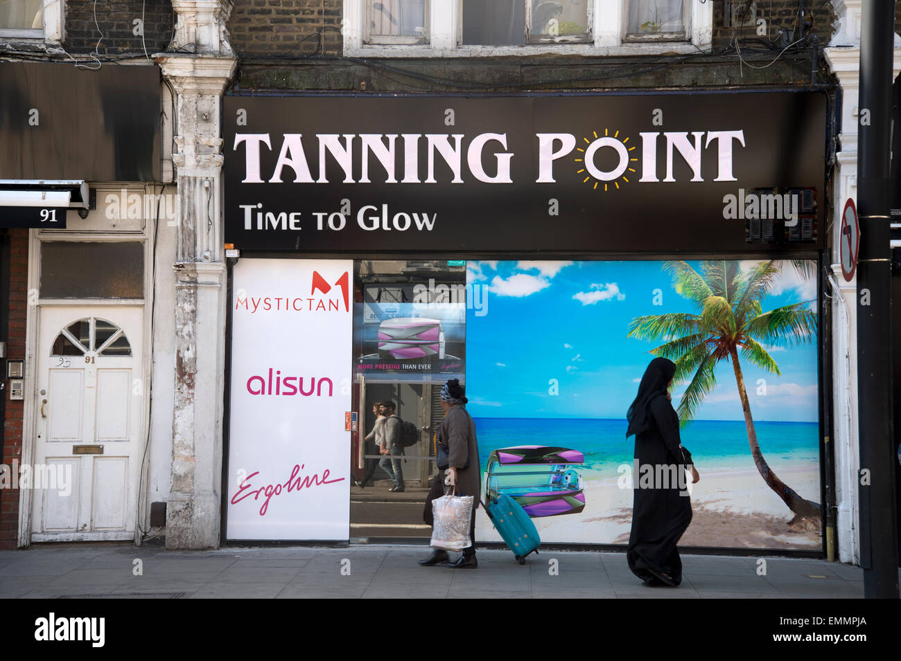 Abbronzante con Palm Tree spiaggia foto murale e persone passato a camminare sul marciapiede compresi donna in abito islamico Foto Stock