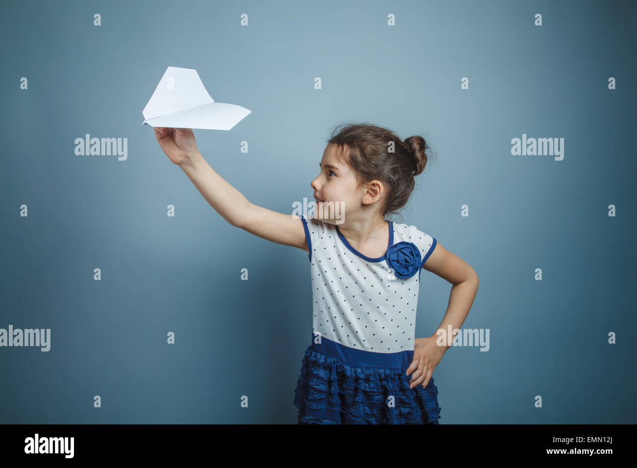 Una bambina di sette anni aspetto europeo brunette tenendo un aeroplano di carta su uno sfondo grigio, la gioia di volare Foto Stock