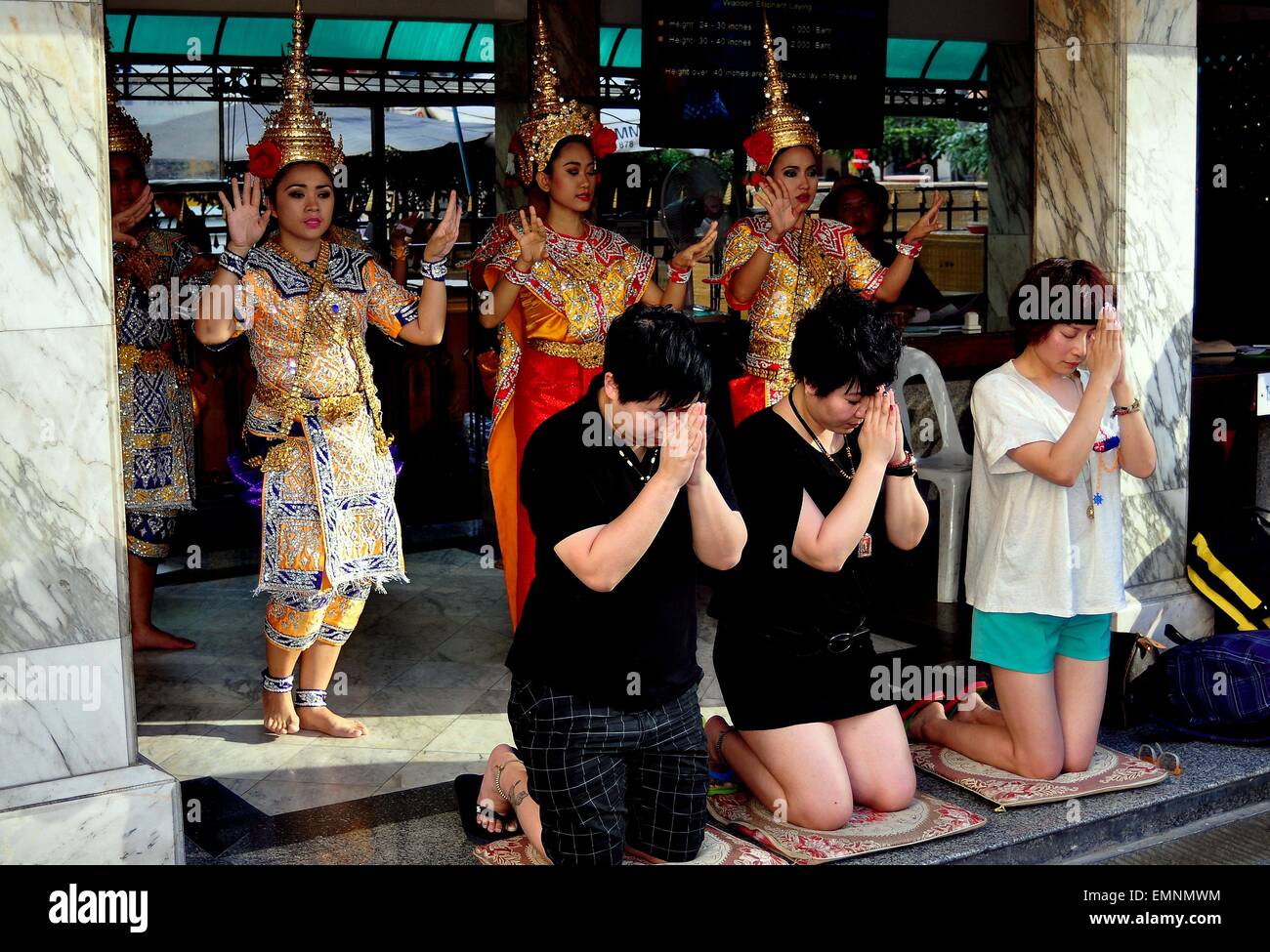 Bangkok, Thailandia: Thai buddisti inginocchiato con le mani giunte in preghiera davanti ad un gruppo di ballerini Khong al Santuario di Erawan Foto Stock