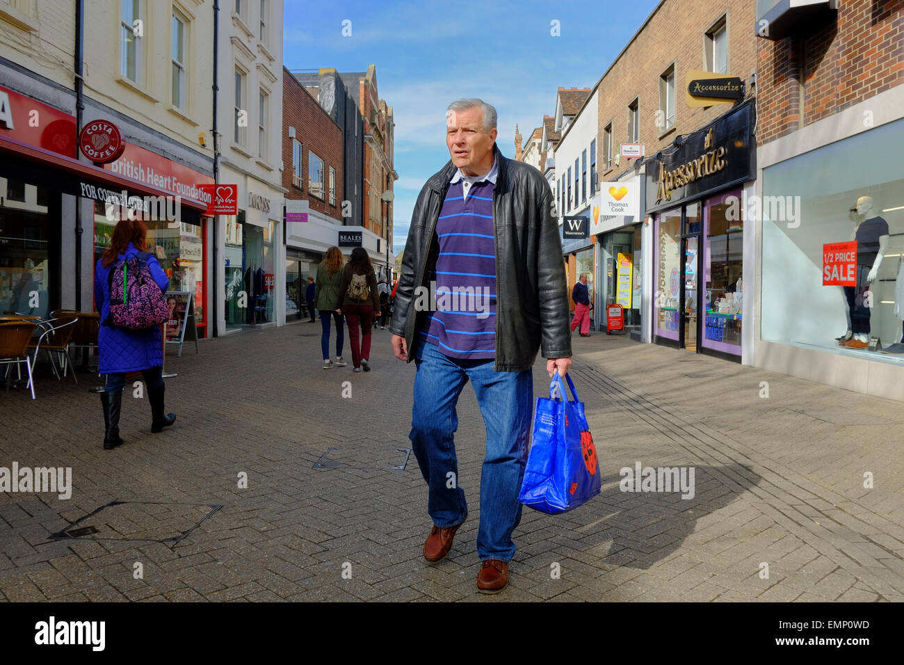 Grigio uomo dai capelli trasportano shopping bag su high street Foto Stock