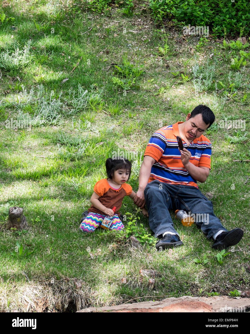 Un padre ispanica scatta foto con il suo telefono cellulare di sua figlia piccola in un parco pubblico. Oklahoma, Stati Uniti d'America Foto Stock