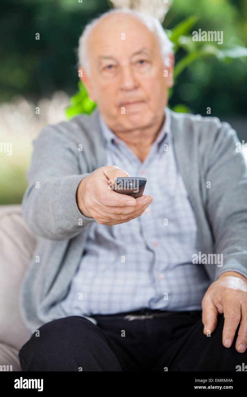 Uomo anziano utilizzando il telecomando mentre è seduto sul lettino Foto Stock