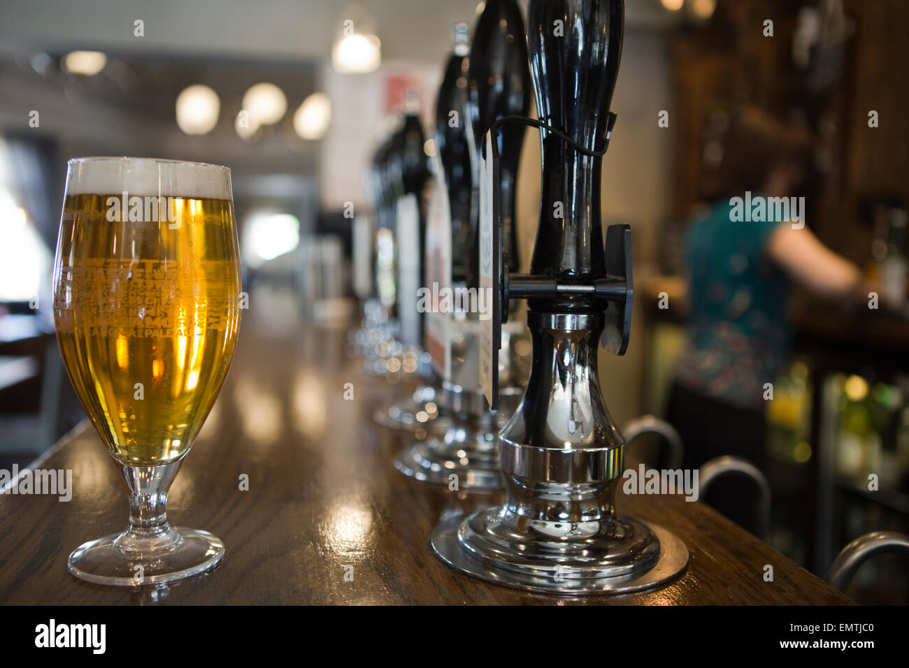 Una pinta di birra in un pub con un membro del personale dietro il bar Foto Stock