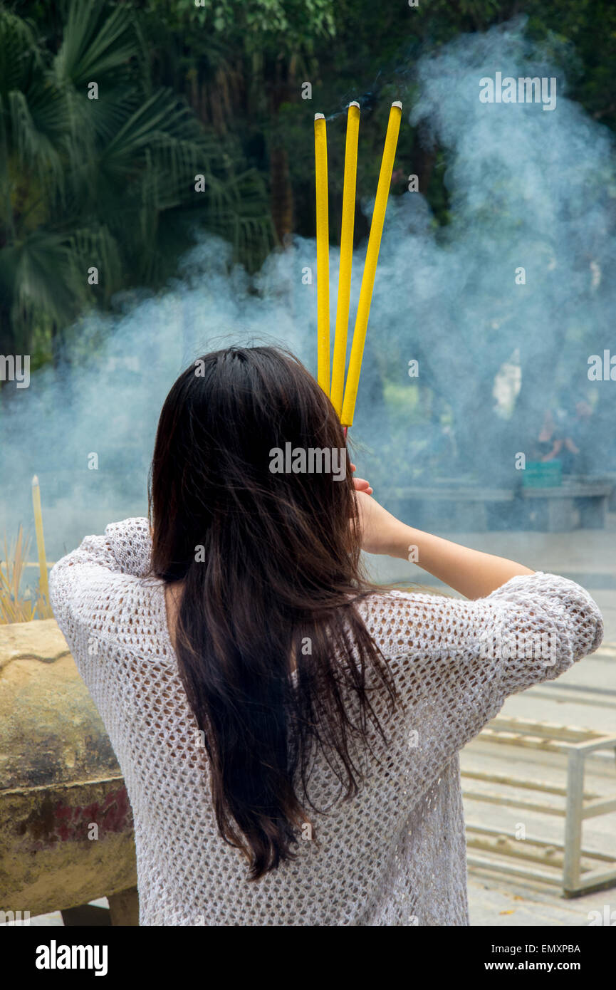 Pregando donna azienda tre bastoncini di incenso davanti al suo volto Foto Stock