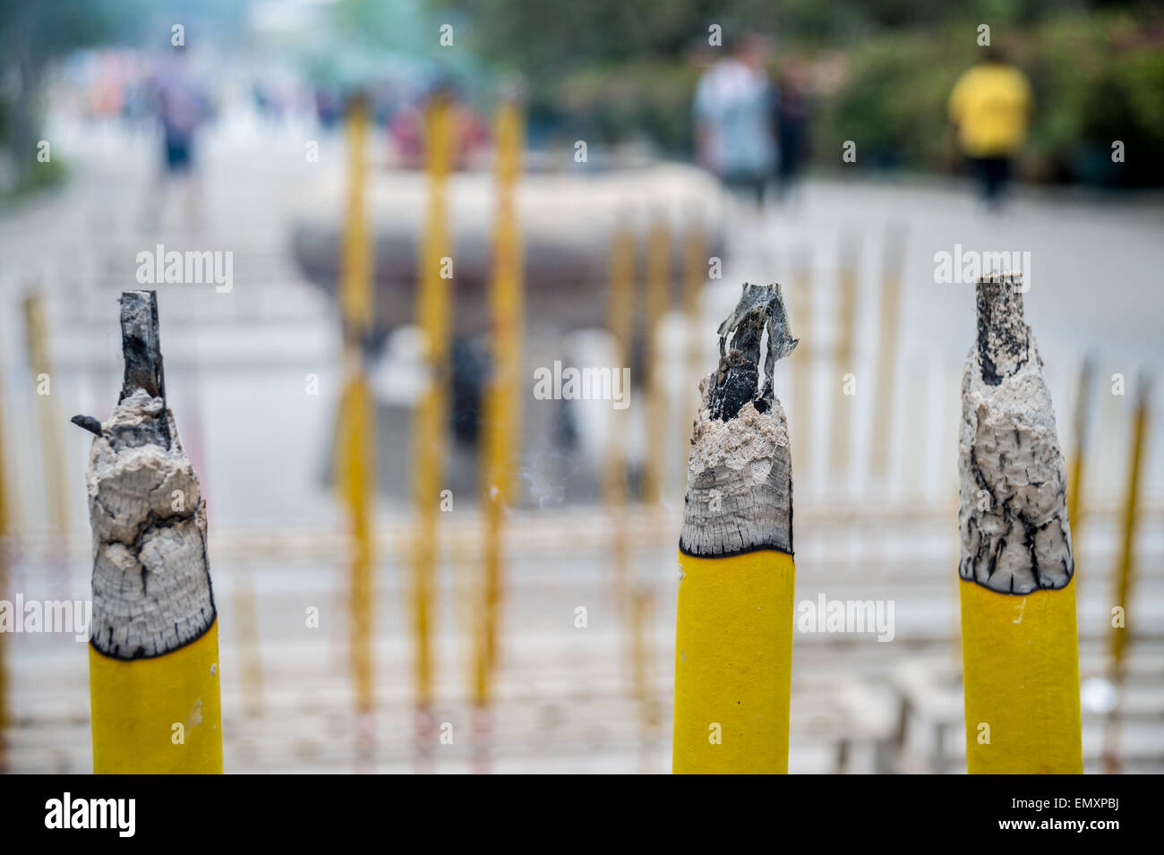 Tre grandi bastoni di incenso bruciare nel tempio cinese con persone sfocate in background Foto Stock