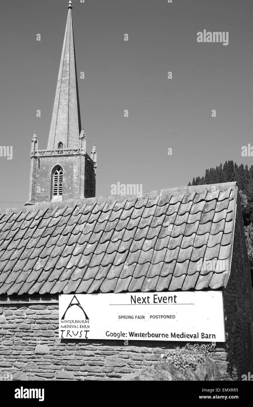 Prossimo evento segno per Winterbourne fienile medievale con chiesa parrocchiale dietro Foto Stock