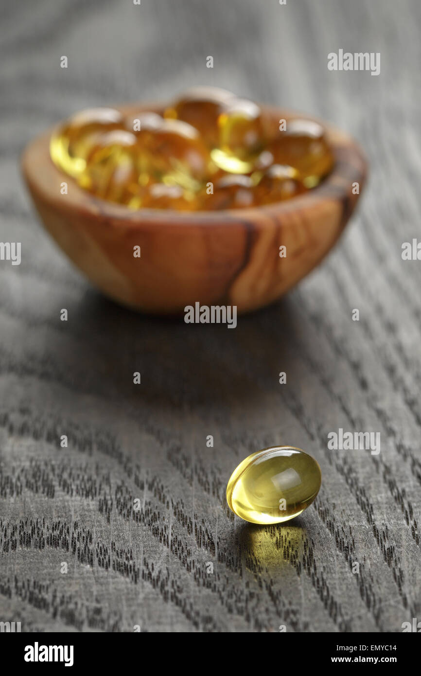 Olio di pesce capsule in ciotola di legno su un tavolo di legno Foto Stock