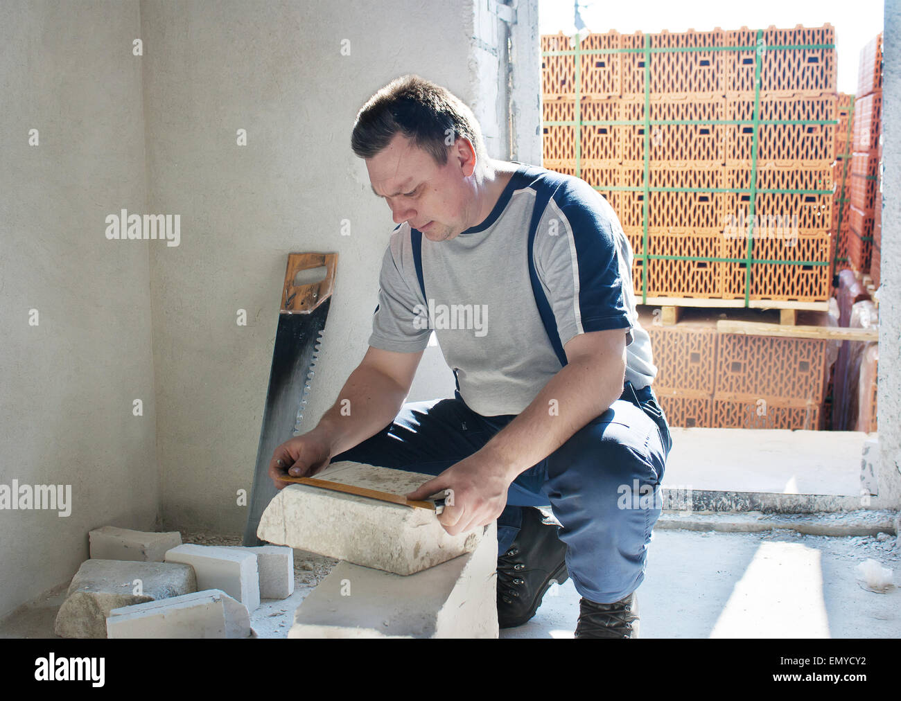 Uomo di mezza età lavoratore in pantaloni blu e grigio t-shirt le misure del righello in mattoni di silicato in camera della nuova casa Foto Stock