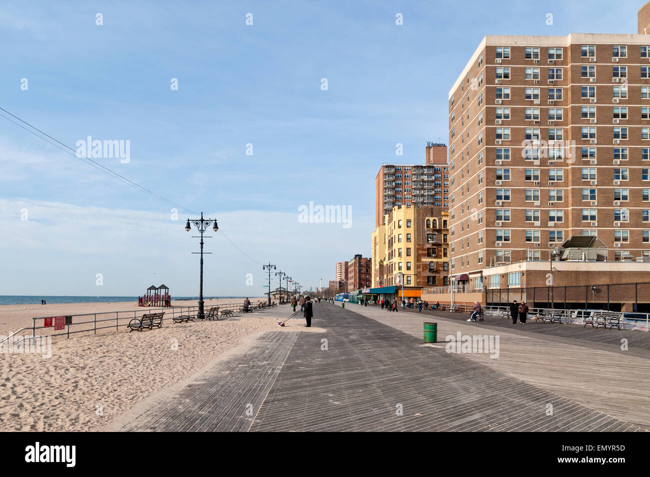 La gente seduta sulle panchine al sole e camminare davanti a un edificio con appartamenti sul lungomare presso la spiaggia di Brighton, Brooklyn NY Foto Stock