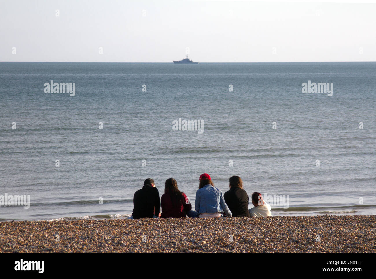 Un gruppo sulla spiaggia di Brighton, con una nave da guerra all'orizzonte Foto Stock