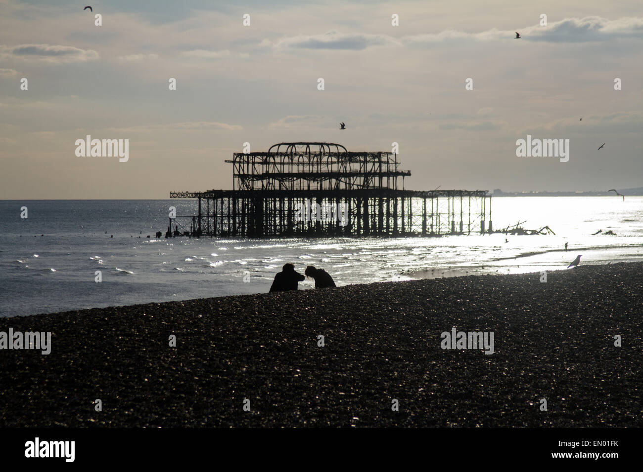 Un giovane sulla spiaggia di Brighton, con i resti del distrutto Molo Ovest in background Foto Stock