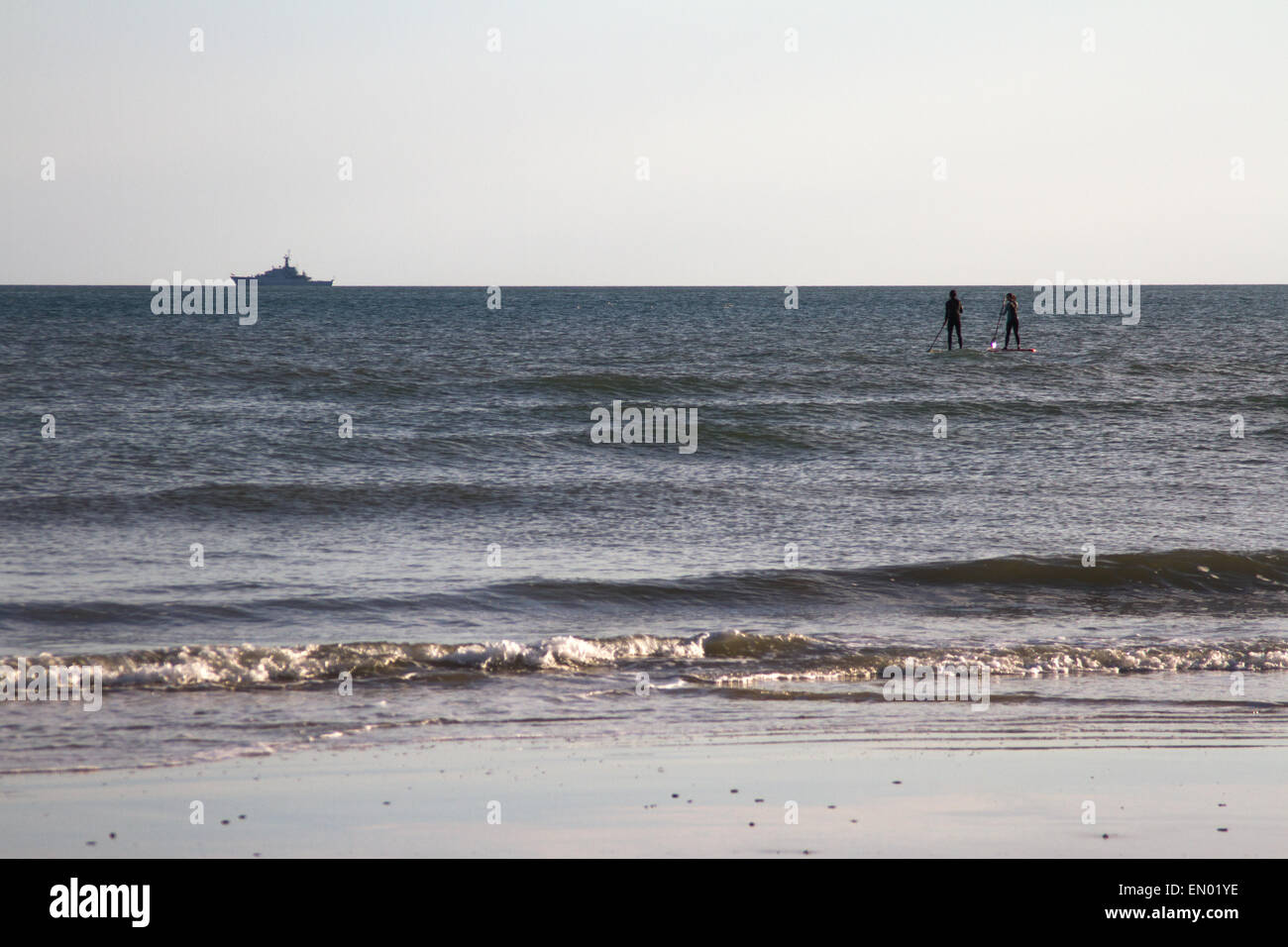 Surfers testa fuori al mare di spiaggia di Brighton, con una nave da guerra all'orizzonte Foto Stock