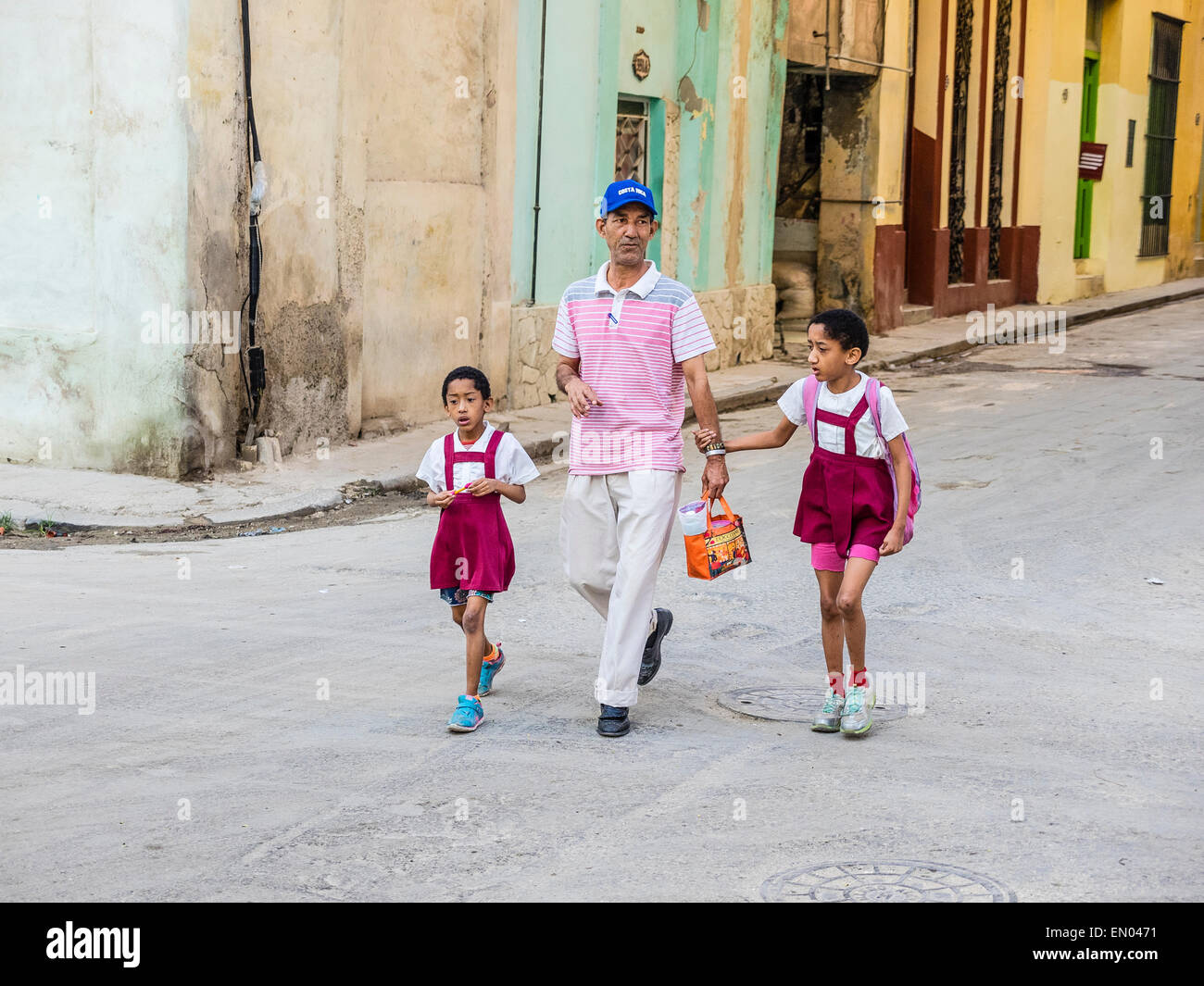 Un ispanico padre cubano passeggiate le sue due giovani figlie che sono vestiti in uniformi di scuola, attraverso la strada per la scuola primaria Foto Stock