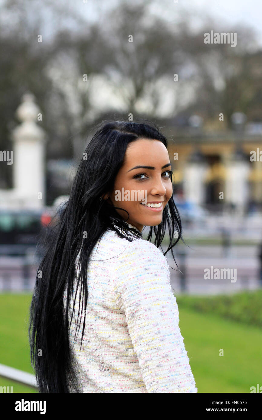 Un felice e sorridente giovane donna con lunghi capelli scuri e la carnagione di oliva fuori Buckingham Palace a Londra. Foto Stock