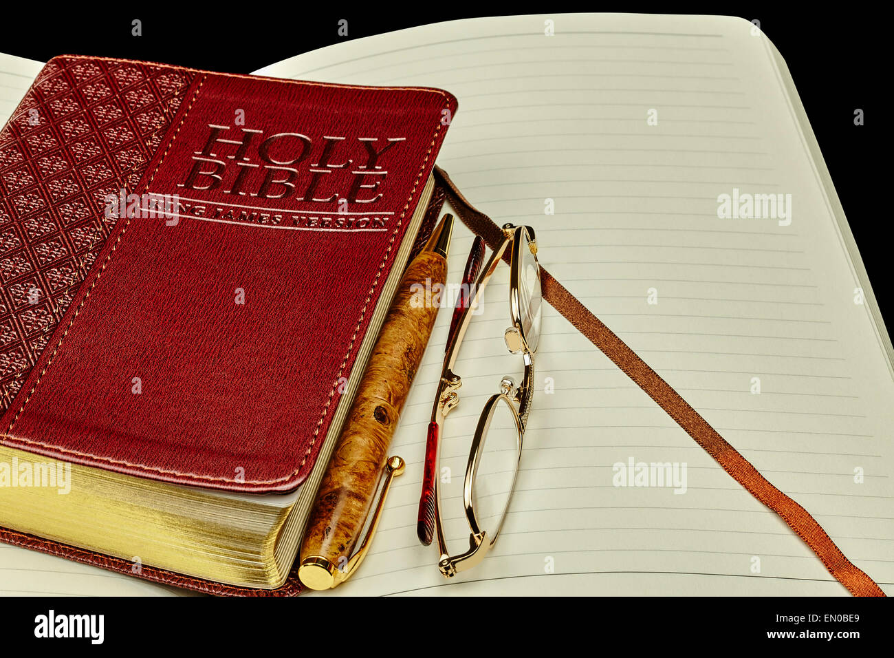 Generico chiuso libro della Bibbia con lo studio personale ufficiale e penna di business con gli occhiali da lettura su sfondo nero Foto Stock
